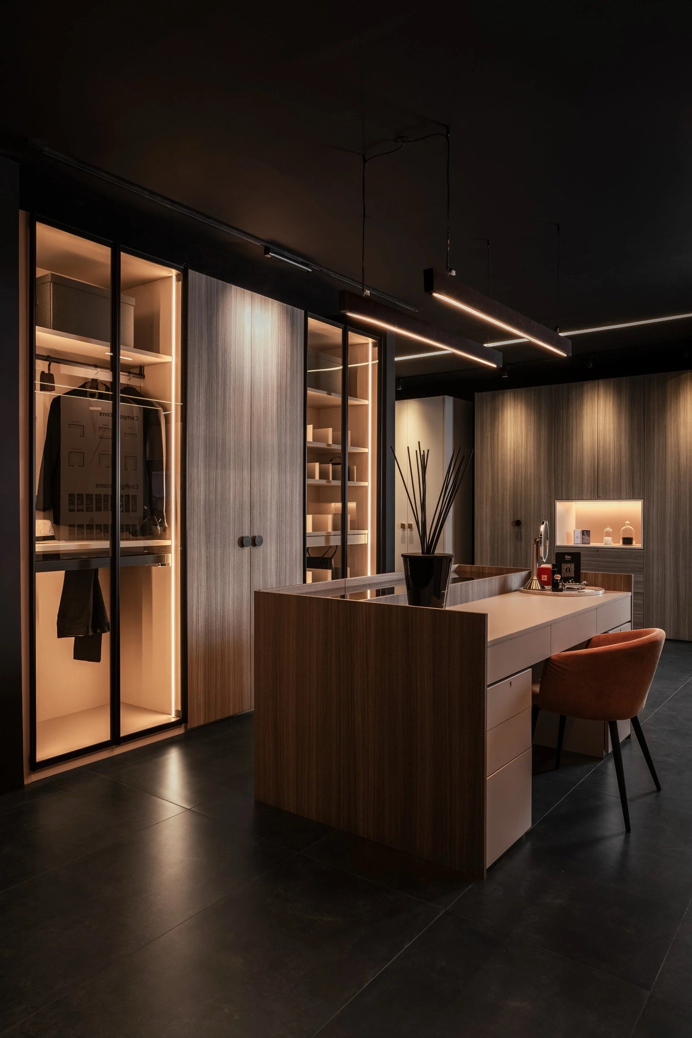 Be: by Woodex showroom — walk-in wardrobe with a lit glass-door display island and warm moody lighting